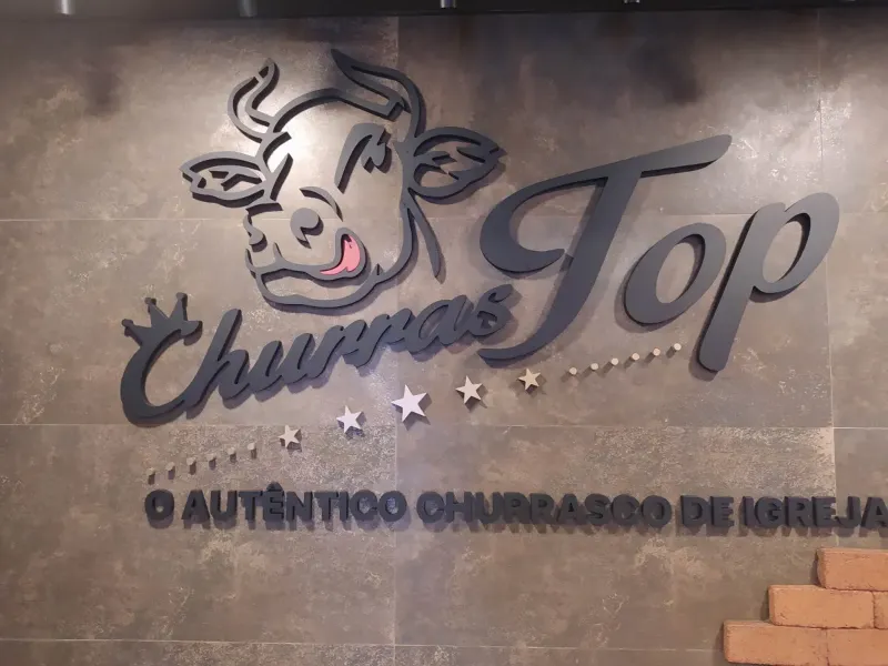 Letras do logotipo ChurrasTop recortadas em vinil, aplicadas numa parede de tijolinho